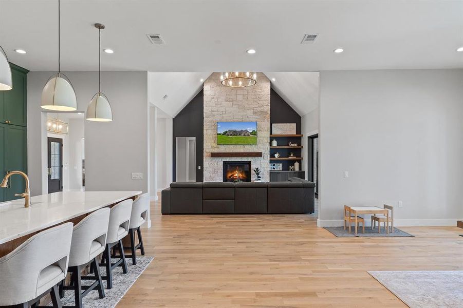 Living room featuring an inviting chandelier, a stone fireplace, built in features, and light hardwood / wood-style floors