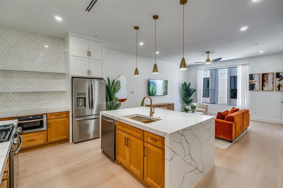 Model Home Kitchen with decorative backsplash, appliances with stainless steel finishes, open floor plan, brown cabinetry, and light wood-style flooring