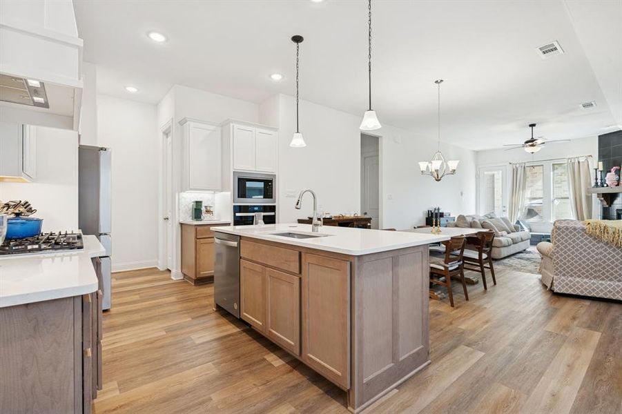 Kitchen featuring a chandelier, open floor plan, hanging light fixtures, ventilation hood, and a ceiling fan Kitchen featuring a chandelier, open floor plan, hanging light fixtures, ventilation hood, and a ceiling fan