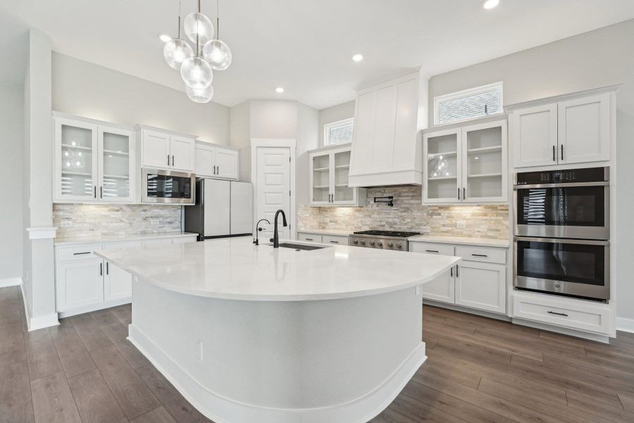 Kitchen featuring white cabinets, a sink, a center island with sink, tasteful backsplash, and appliances with stainless steel finishes Kitchen featuring white cabinets, a sink, a center island with sink, tasteful backsplash, and appliances with stainless steel finishes