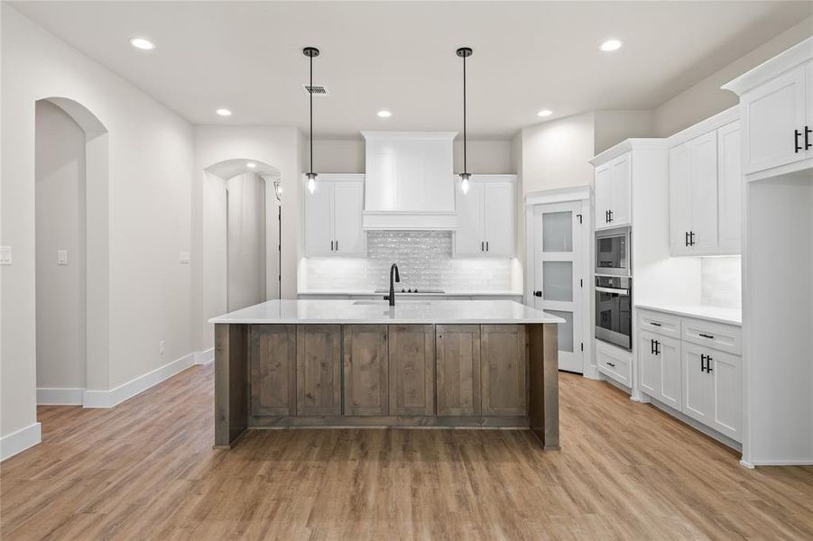 Two tone kitchen with a kitchen island with sink, stainless steel appliances, light stone counters, arched walkways, and dual tone cabinets