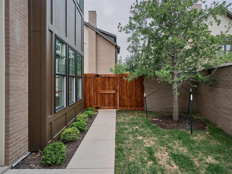 Private outdoor space featuring a mature tree, manicured lawn, and brick perimeter wall