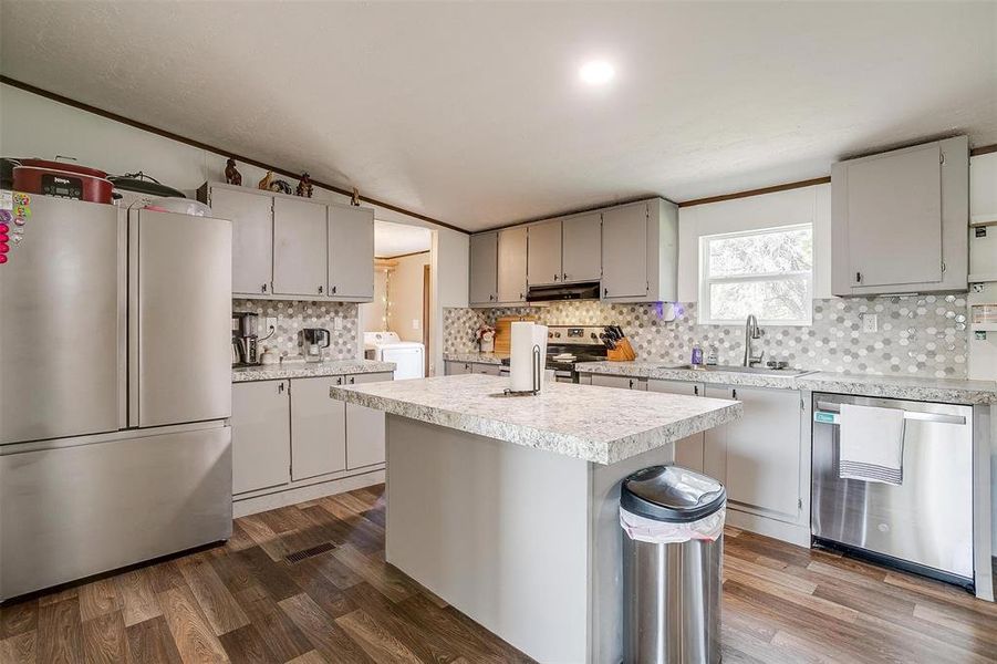 Kitchen featuring appliances with stainless steel finishes, dark hardwood / wood-style floors, a center island, independent washer and dryer, and sink