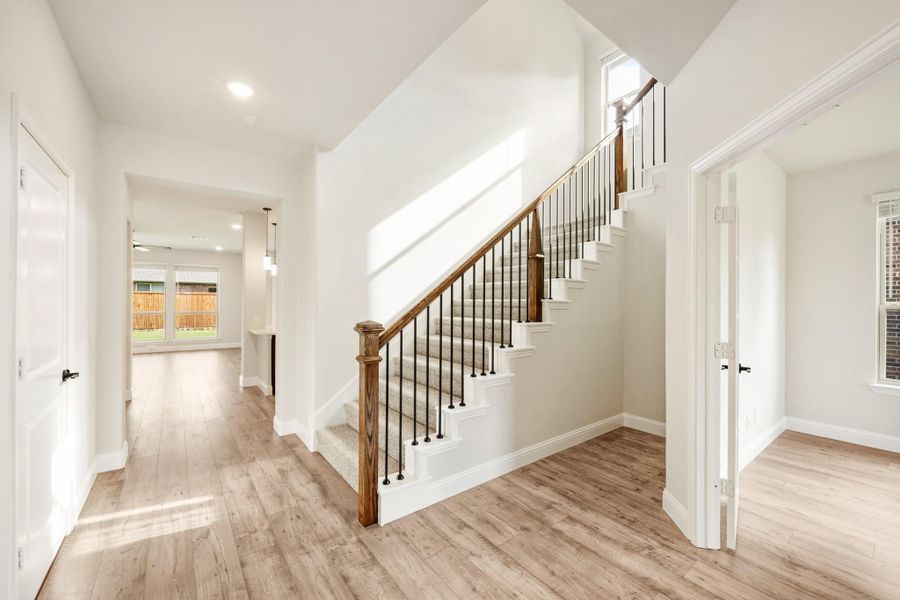 Bright entryway with wood staircase, metal balusters, and light hardwood floors leading to open living area