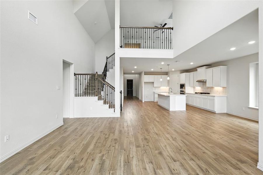 Unfurnished living room with light wood-style floors, a towering ceiling, stairs, and recessed lighting