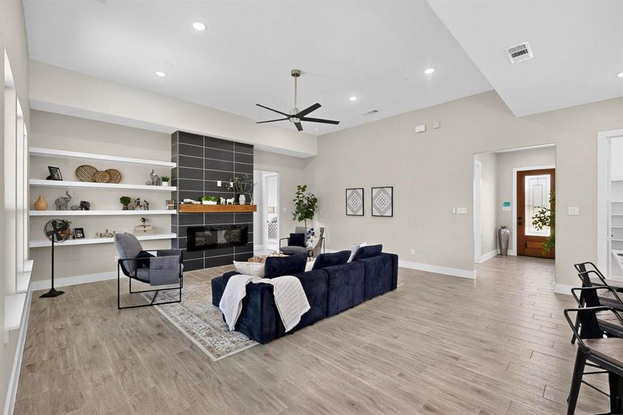 Living area with built in features, light wood finished floors, recessed lighting, a fireplace, and ceiling fan