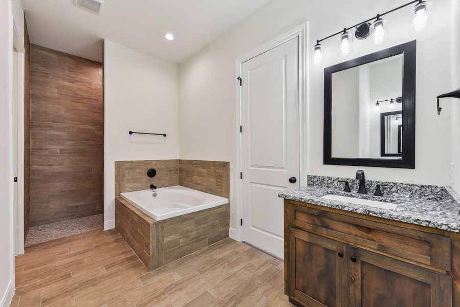 Full bath featuring visible vents, wood finished floors, a tile shower, a bath, and vanity Full bath featuring visible vents, wood finished floors, a tile shower, a bath, and vanity
