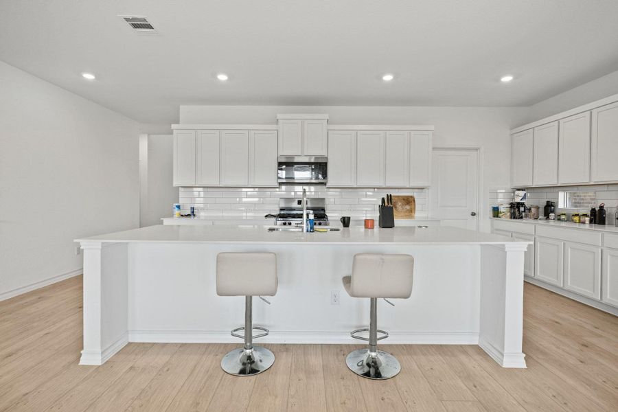 Kitchen featuring an island with sink, white cabinets, a breakfast bar, backsplash, and recessed lighting
