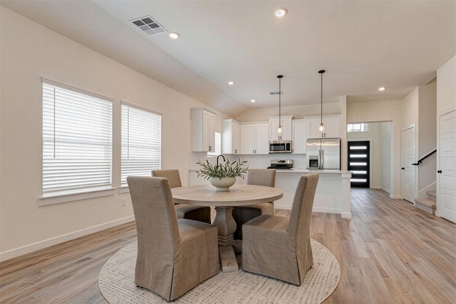 This expansive kitchen and dining space offers a bright, open layout perfect for gatherings. Featuring white cabinetry, sleek hardware, and stainless steel appliances, the kitchen exudes contemporary elegance. Large windows invite natural light, while the open floor plan allows for effortless interaction between cooking, dining, and relaxing areas. This photo is virtually staged.