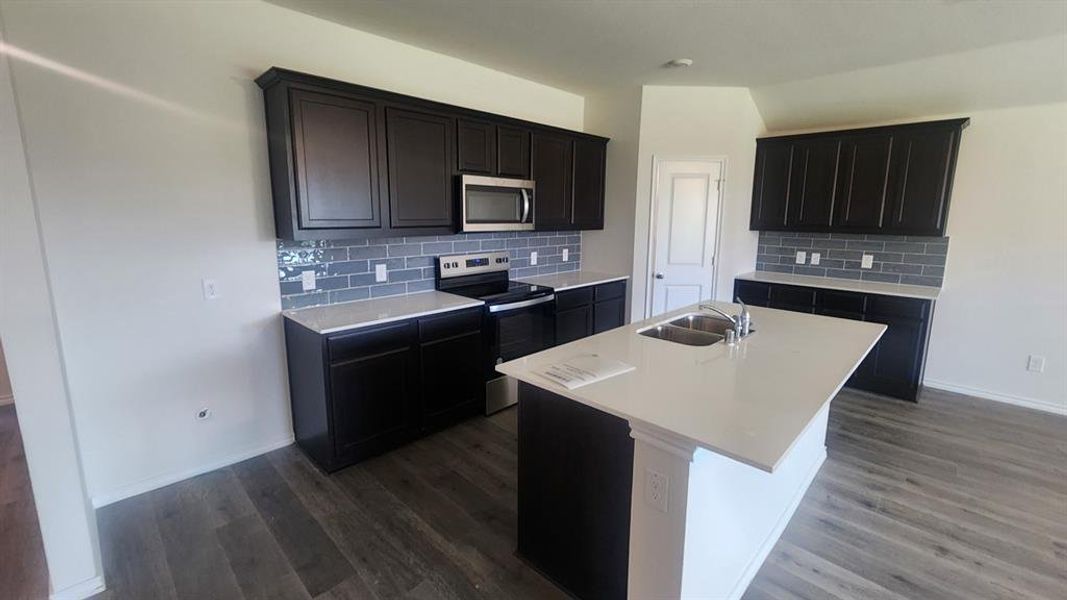 Kitchen featuring dark wood cabinetry, light countertops, subway tile backsplash, and wood-finish flooring