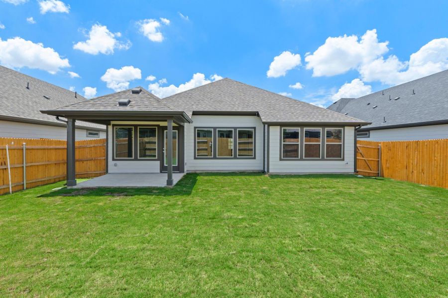 A neatly manicured lawn extends from a covered patio, framed by a sturdy wood fence.