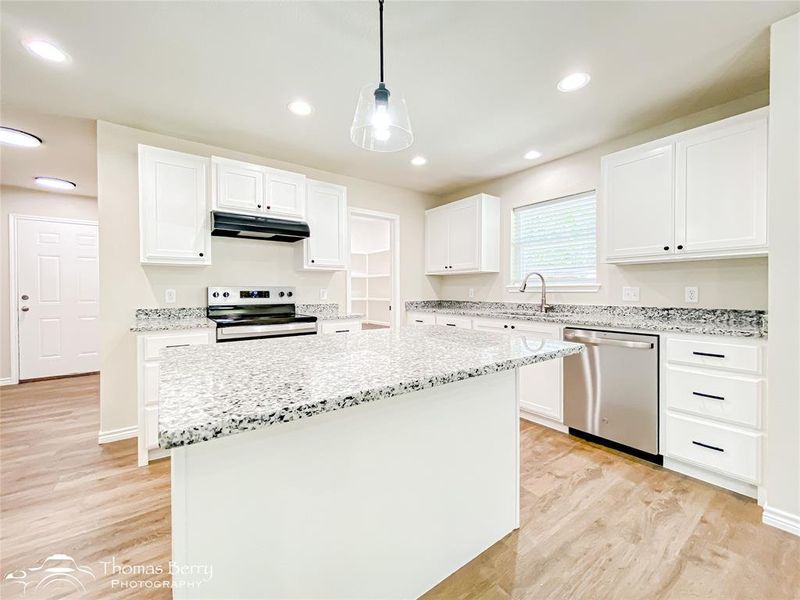 Kitchen with white cabinets, hanging light fixtures, light stone counters, appliances with stainless steel finishes, and recessed lighting Kitchen with white cabinets, hanging light fixtures, light stone counters, appliances with stainless steel finishes, and recessed lighting