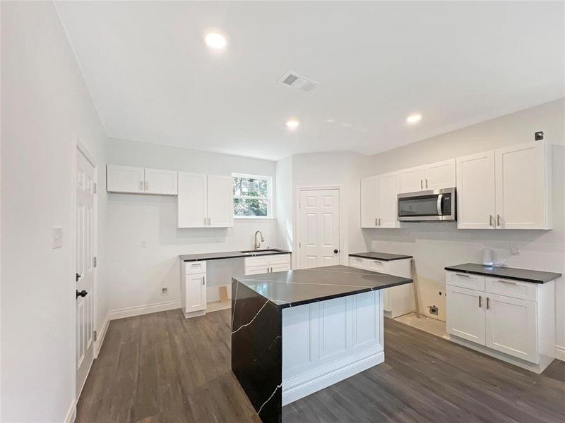 Kitchen with dark wood-type flooring, stainless steel microwave, white cabinetry, a center island, and recessed lighting Kitchen with dark wood-type flooring, stainless steel microwave, white cabinetry, a center island, and recessed lighting