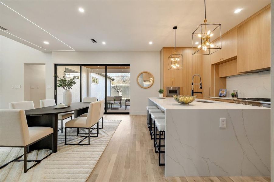 Kitchen with pendant lighting, a kitchen bar, light brown cabinets, an island with sink, and light hardwood / wood-style floors