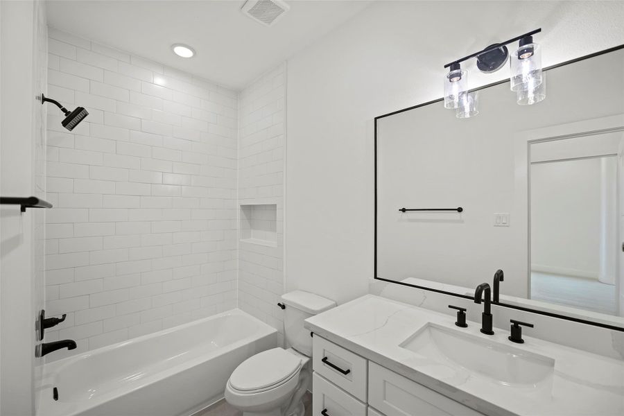This modern bathroom features a sleek design with a white subway-tiled shower and a built-in niche. It includes a bathtub, a stylish vanity with a large mirror, and black fixtures for a contemporary look. The room is well-lit with recessed lighting and a decorative light fixture.