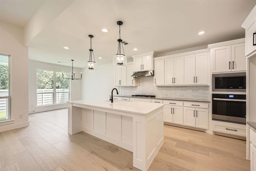 Kitchen featuring appliances with stainless steel finishes, under cabinet range hood, tasteful backsplash, recessed lighting, and light wood-style flooring