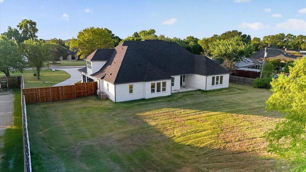 Expansive rear lawn featuring a newly constructed white exterior residence with multiple windows, a dark shingle roof, and a private wood fence Expansive rear lawn featuring a newly constructed white exterior residence with multiple windows, a dark shingle roof, and a private wood fence