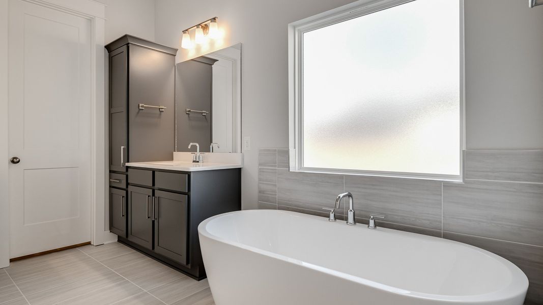 Large tiled bathroom with multiple vanities, glass shower enclosure, and freestanding tub