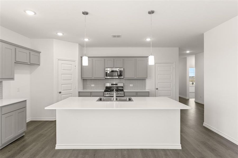 Kitchen featuring appliances with stainless steel finishes, dark hardwood / wood-style flooring, sink, decorative light fixtures, and an island with sink