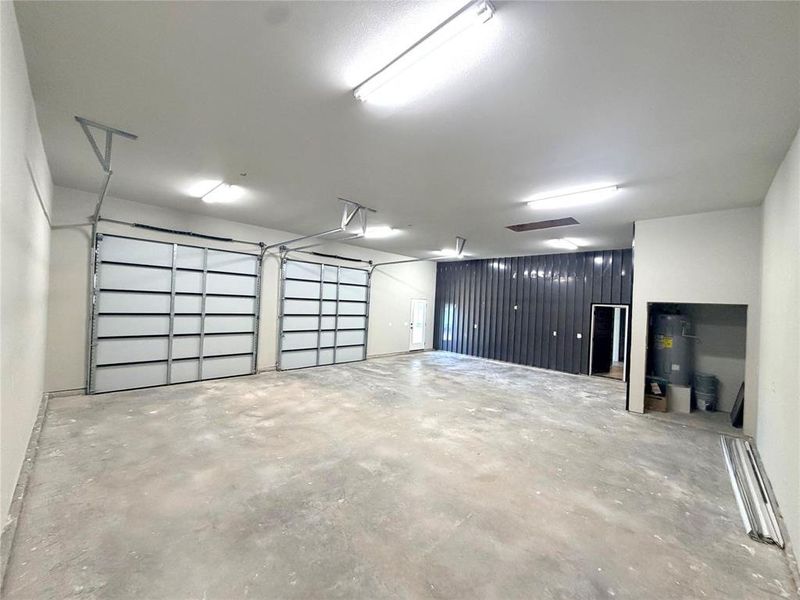Spacious interior featuring two overhead doors, exposed concrete flooring, and a corrugated metal accent wall Spacious interior featuring two overhead doors, exposed concrete flooring, and a corrugated metal accent wall