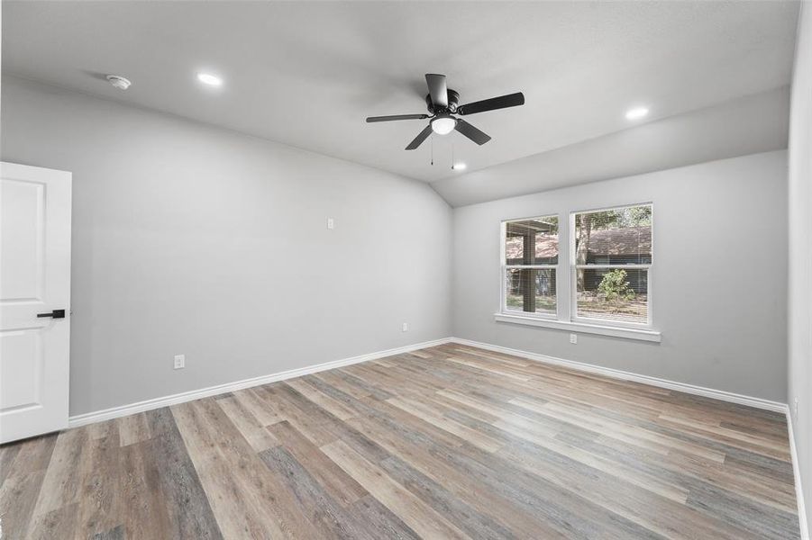 Spacious room featuring wood-finish flooring, light grey walls, and a contemporary ceiling fan Spacious room featuring wood-finish flooring, light grey walls, and a contemporary ceiling fan