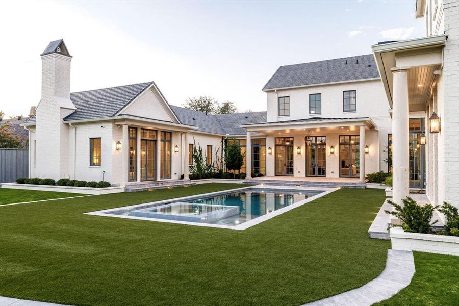 Back of property featuring a patio, a pool with connected hot tub, a lawn, brick siding, and a chimney Back of property featuring a patio, a pool with connected hot tub, a lawn, brick siding, and a chimney