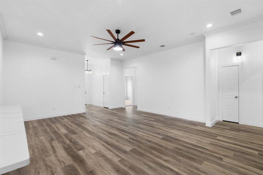 Unfurnished living room with dark wood-type flooring, ceiling fan, and crown molding