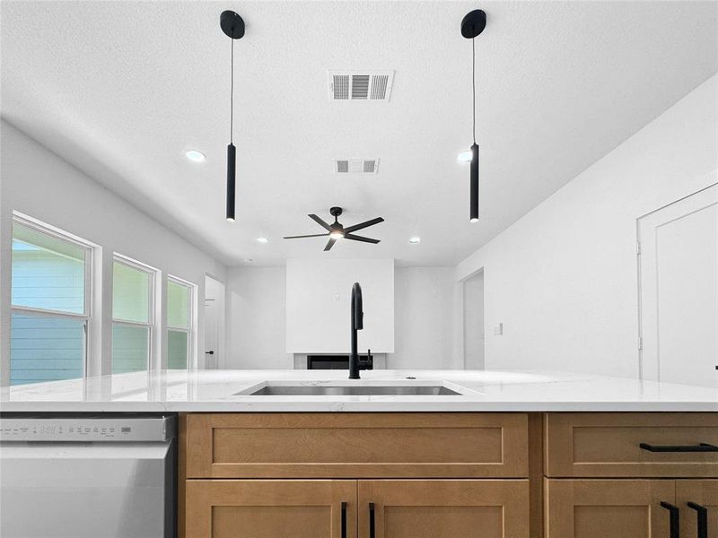 Kitchen with dishwasher, brown cabinets, open floor plan, light stone counters, and hanging light fixtures
