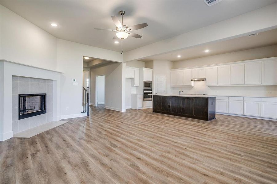 Kitchen with stainless steel appliances, light hardwood / wood-style flooring, a tiled fireplace, a center island with sink, and white cabinets