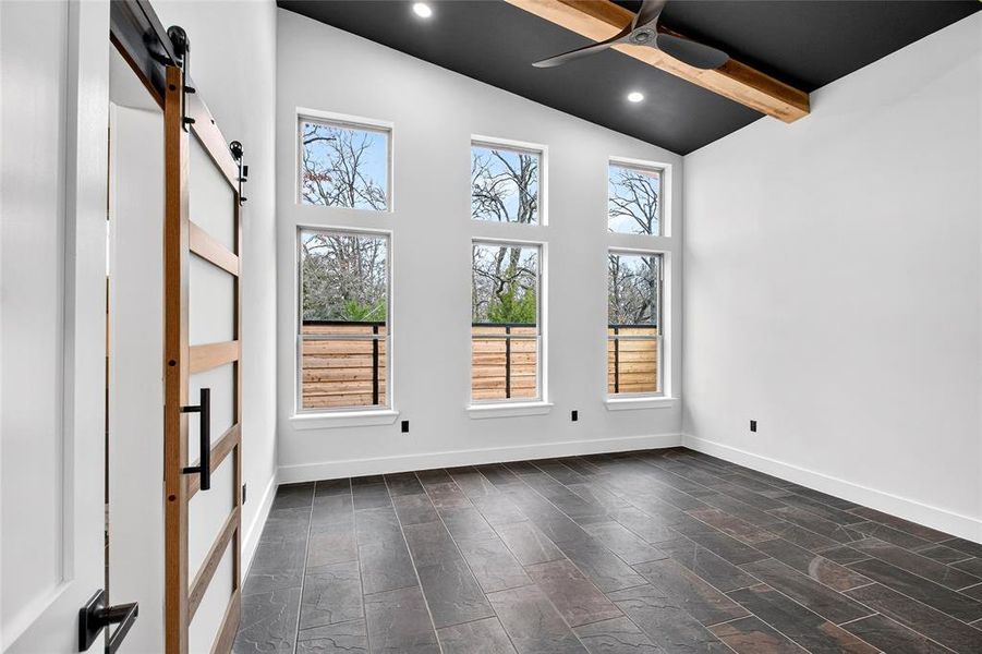 Empty room with a barn door, vaulted ceiling, recessed lighting, and ceiling fan