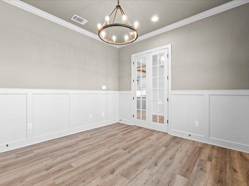 Empty room featuring a wainscoted wall, a decorative wall, light wood-style floors, ornamental molding, and a chandelier Empty room featuring a wainscoted wall, a decorative wall, light wood-style floors, ornamental molding, and a chandelier