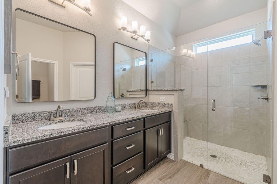 Full bathroom with a stall shower, double vanity, and wood finished floors