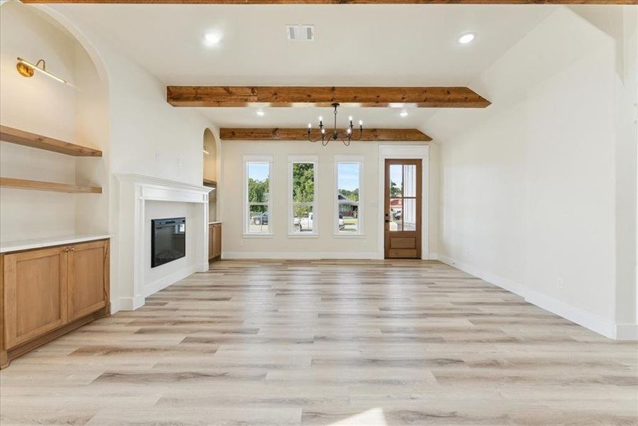 Unfurnished living room featuring a glass covered fireplace, light wood finished floors, recessed lighting, beam ceiling, and a chandelier