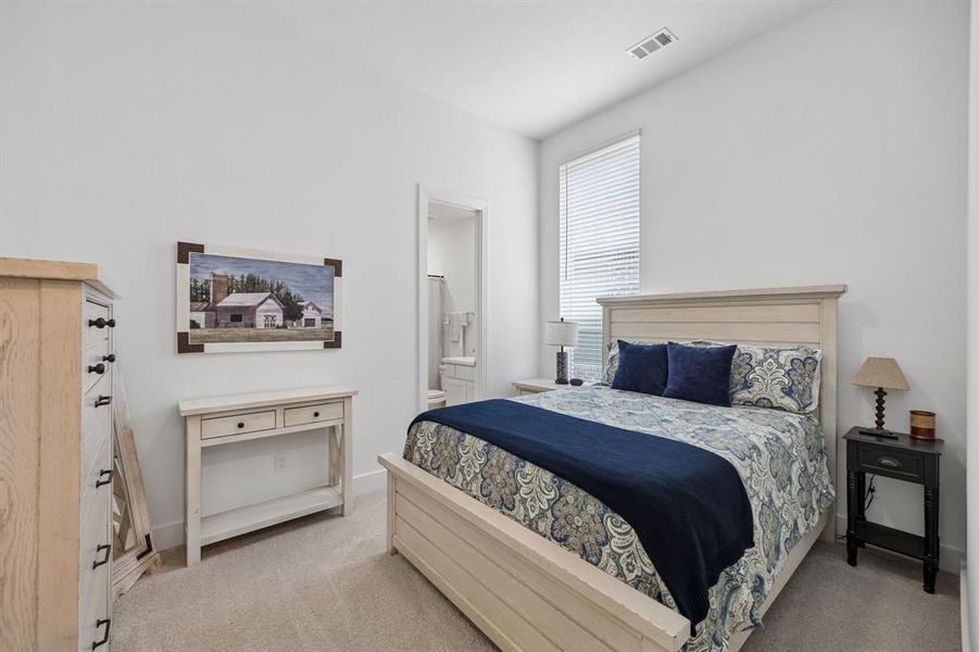 Carpeted bedroom with a window featuring blinds, a built-in air vent, and a doorway opening to a bathroom