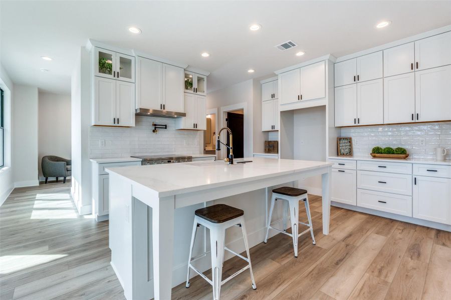 Kitchen with white cabinets, a breakfast bar, glass insert cabinets, light wood-style floors, and recessed lighting