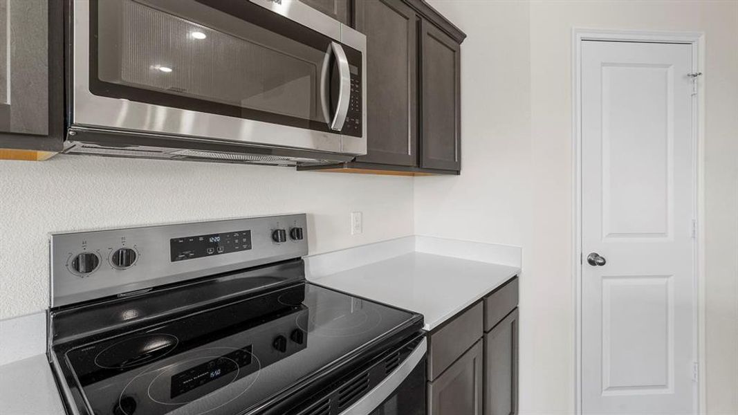 Kitchen featuring stainless steel range and microwave, dark wood-finish cabinetry, and light-toned countertops