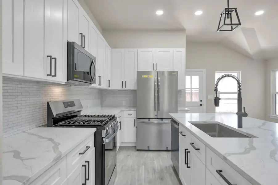 A chef’s dream featuring bright white cabinetry, sleek quartz countertops with waterfall potential, a designer subway tile backsplash, and premium stainless steel appliances.