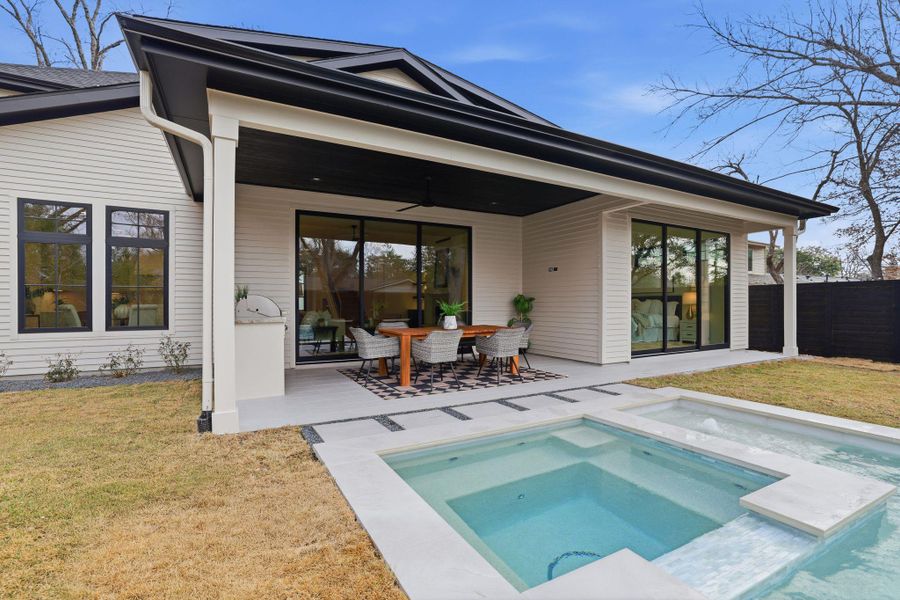 Back of property with ceiling fan, a patio area, outdoor dining area, and an in-ground hot tub