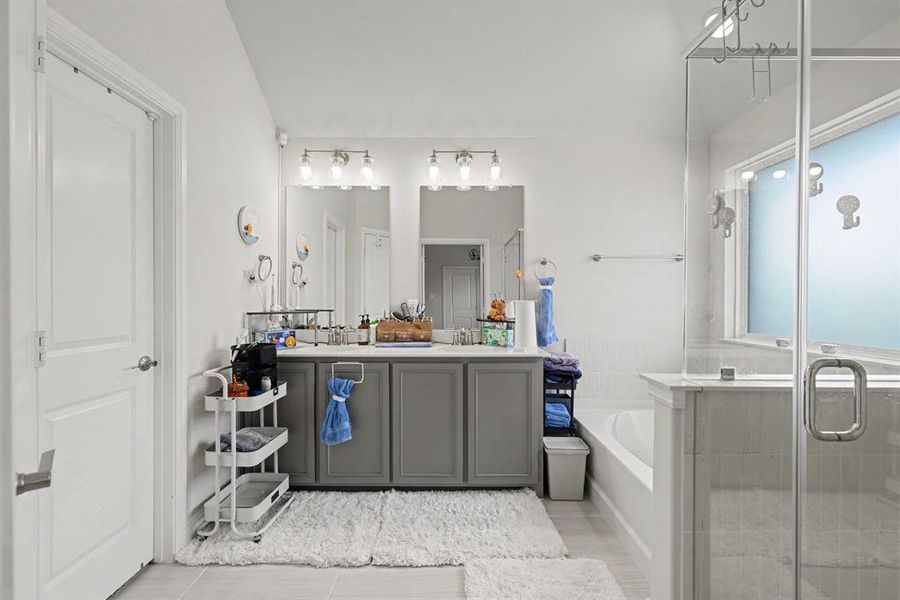 Bathroom featuring a dual vanity with gray cabinetry, a built-in tub, and a glass-enclosed shower