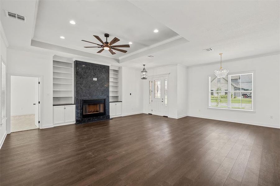 Unfurnished living room with a tray ceiling, ornamental molding, a chandelier, dark wood-type flooring, and a premium fireplace Unfurnished living room with a tray ceiling, ornamental molding, a chandelier, dark wood-type flooring, and a premium fireplace