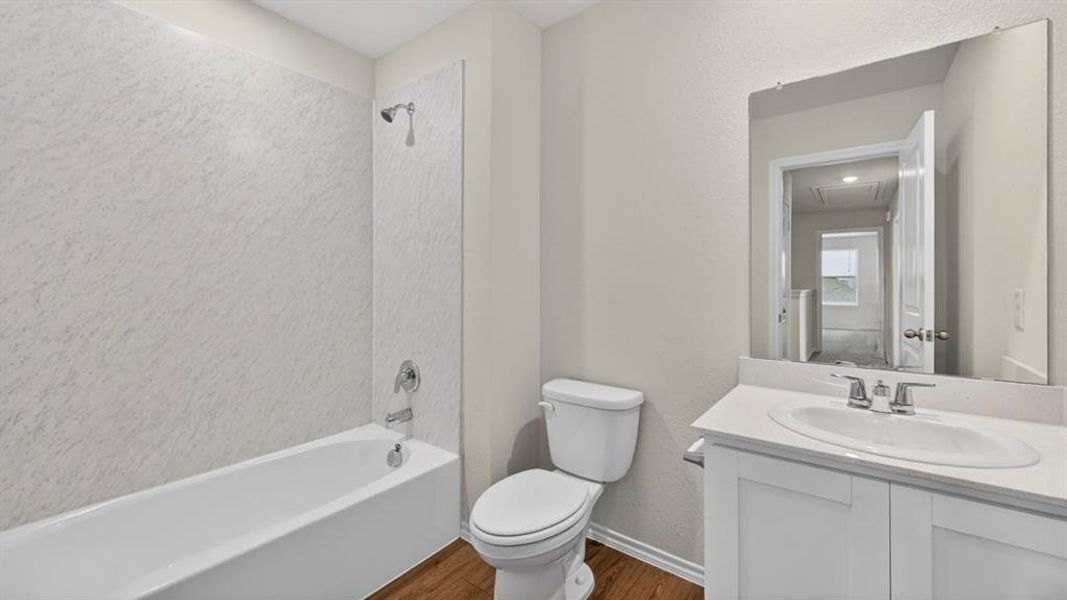 Bathroom featuring a white bathtub with a textured surround, a white vanity with an integrated sink, a large wall-mounted mirror, wood-finish flooring, and chrome fixtures