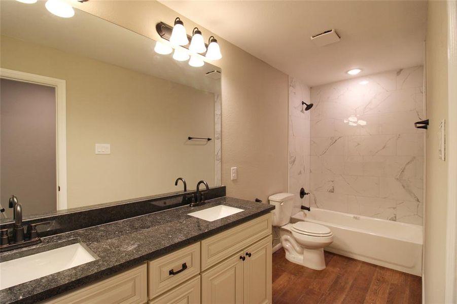 Bathroom with dark wood-type flooring,  shower combination, double vanity, and recessed lighting