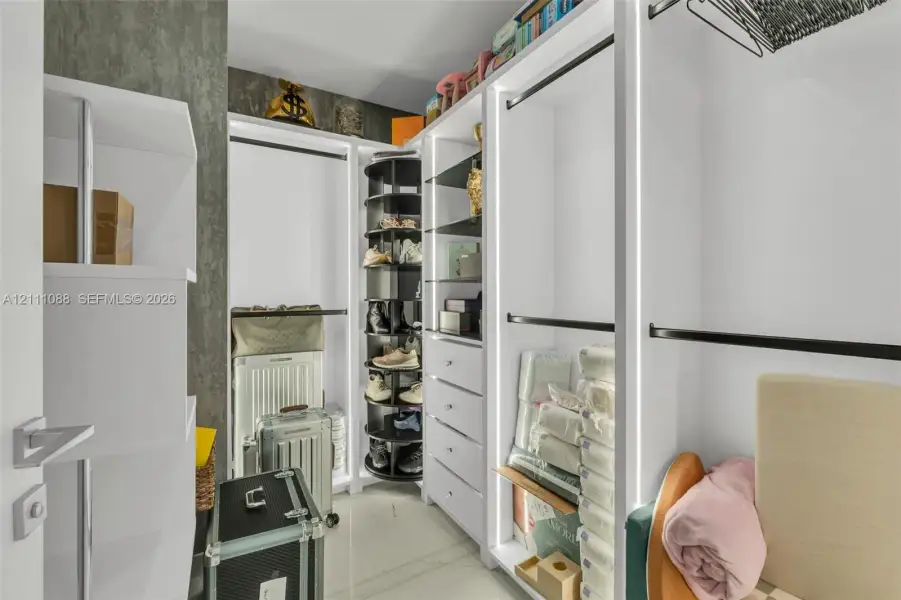 Customized storage system featuring white built-in cabinetry, integrated LED vertical lighting, a rotating shoe rack, multiple drawers, and hanging rods Customized storage system featuring white built-in cabinetry, integrated LED vertical lighting, a rotating shoe rack, multiple drawers, and hanging rods
