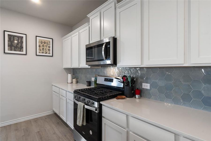 Kitchen with appliances with stainless steel finishes, decorative backsplash, white cabinetry, light wood-style floors, and light stone countertops
