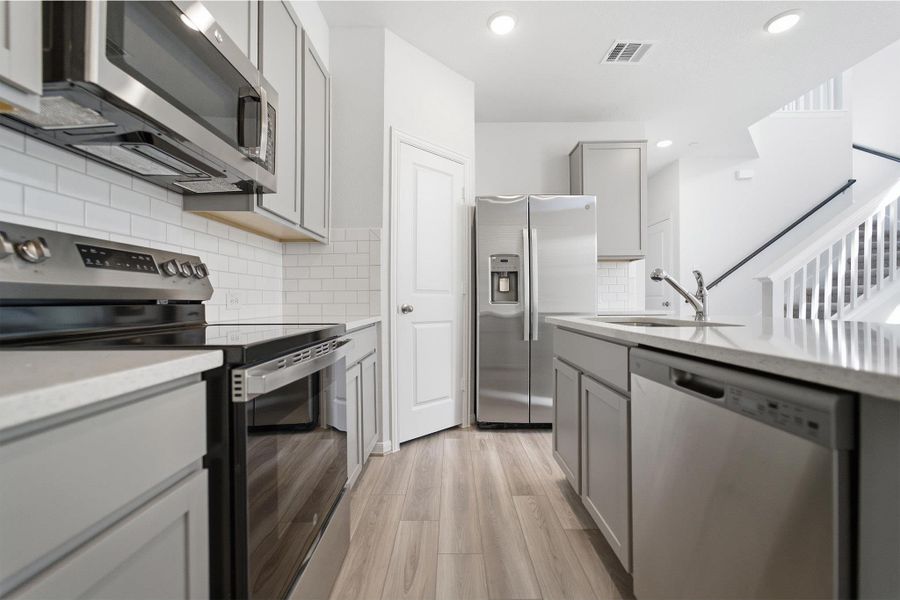 Kitchen with stainless steel appliances, gray cabinetry, light wood finished floors, decorative backsplash, and recessed lighting