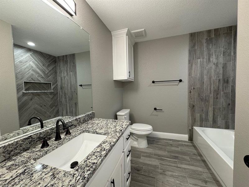 Full bathroom with wood-type flooring, a textured ceiling, toilet, vanity, and tiled shower / bath