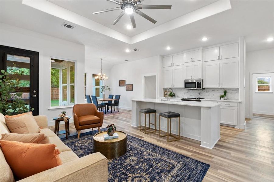 Living room with light wood-type flooring, a raised ceiling, and a wealth of natural light