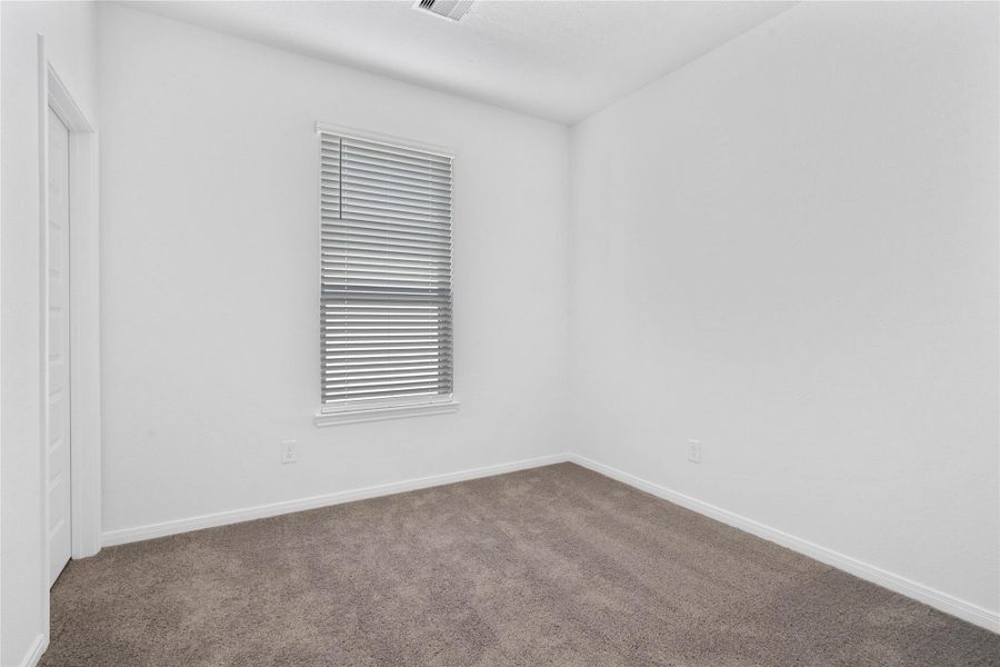 Secondary bedroom, pictured here, features plush carpeting, neutral paint tones, recessed lighting, a large window with privacy blinds, and a walk-in closet.