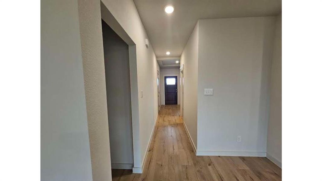 Hallway featuring wood-finish flooring, recessed lighting, white baseboards, light-toned walls, and a dark-paneled door with glass inserts