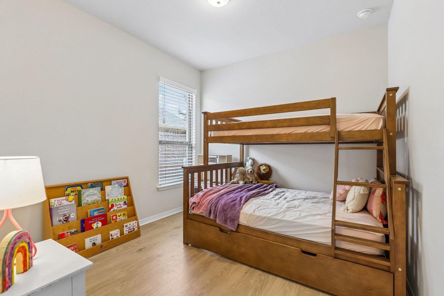 A well-lit bedroom features durable hardwood flooring and a functional bunk bed, maximizing space.